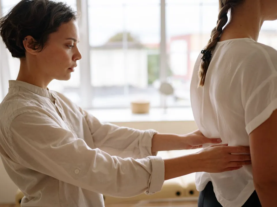 A therapist places her hands on a patient’s back to check alignment.
