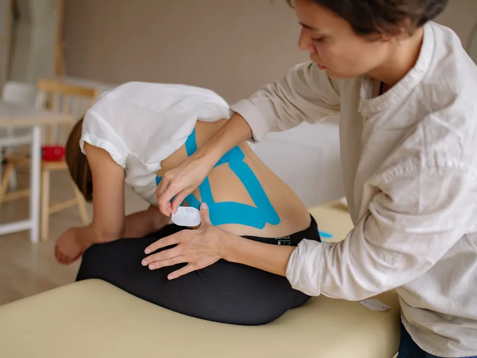 A therapist applies blue kinesiology tape to a patient’s lower back.