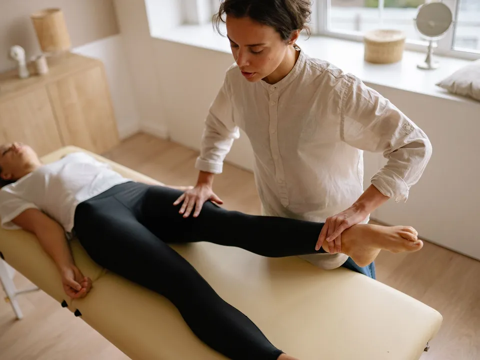 A patient lies on a treatment table while a therapist supports her leg.