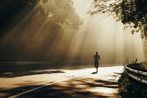 A runner on a tree-lined road with morning sun coming through the branches.