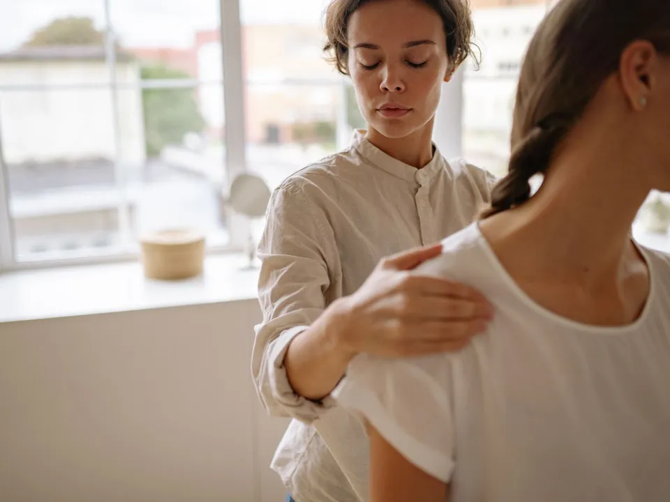 A therapist checks a patient’s shoulder position from behind.
