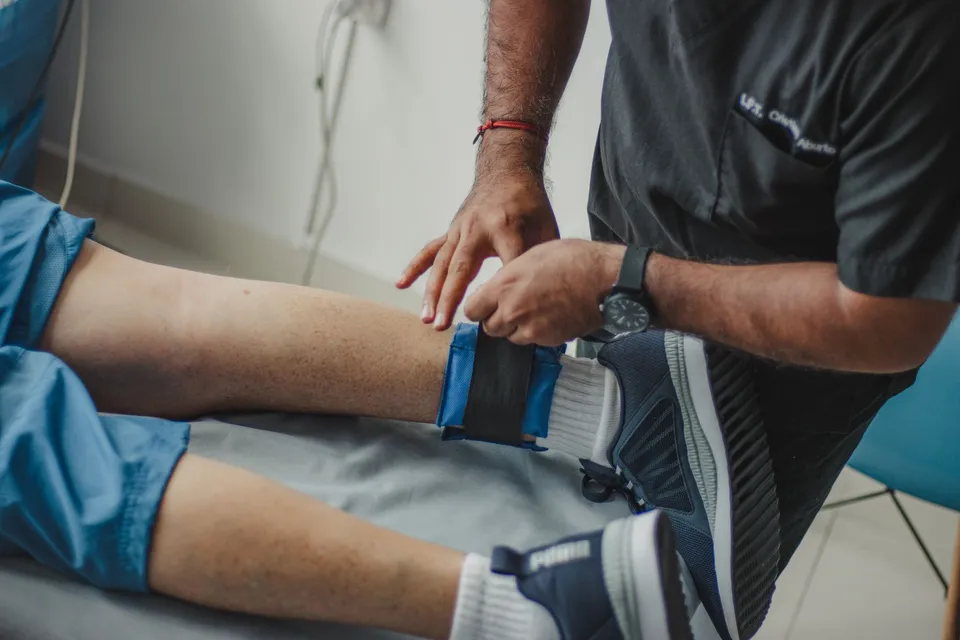 A therapist fastens a support strap around a patient’s knee.