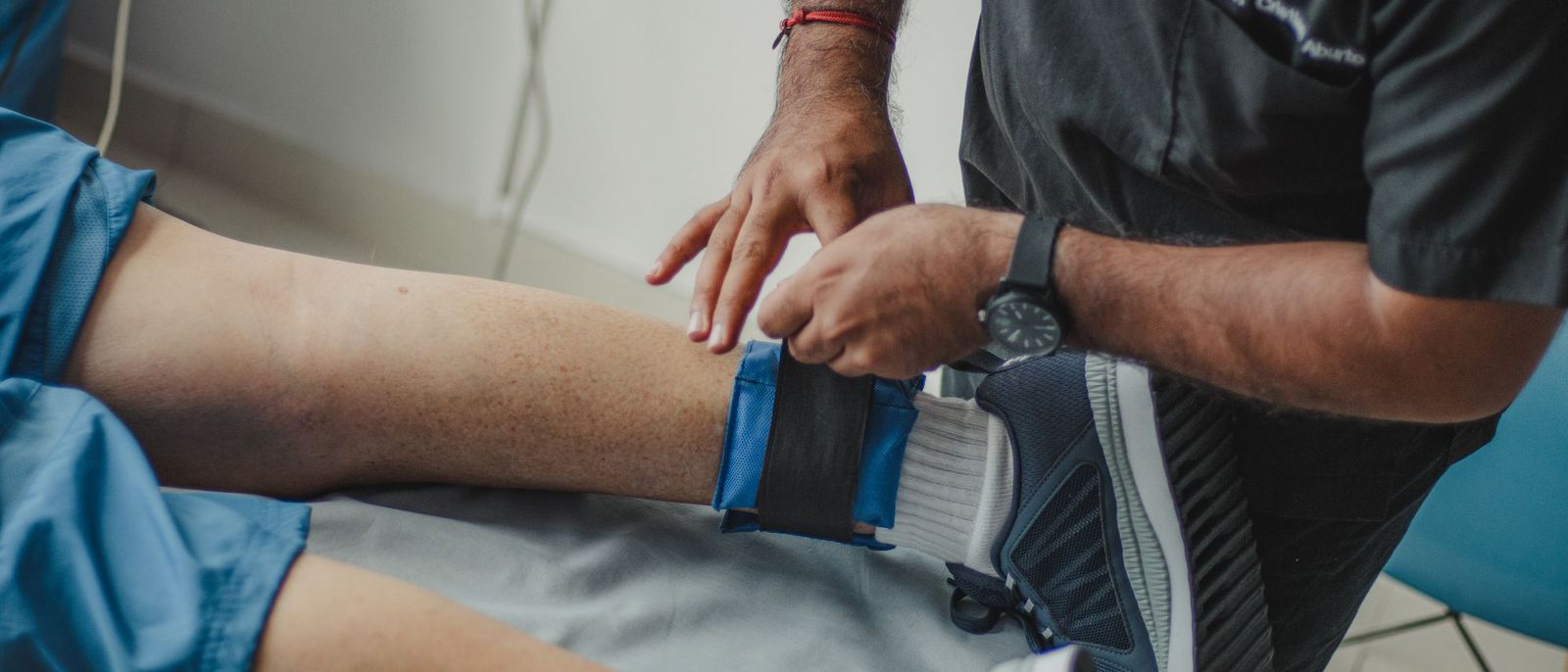 A therapist fastens a support strap around a patient’s knee.