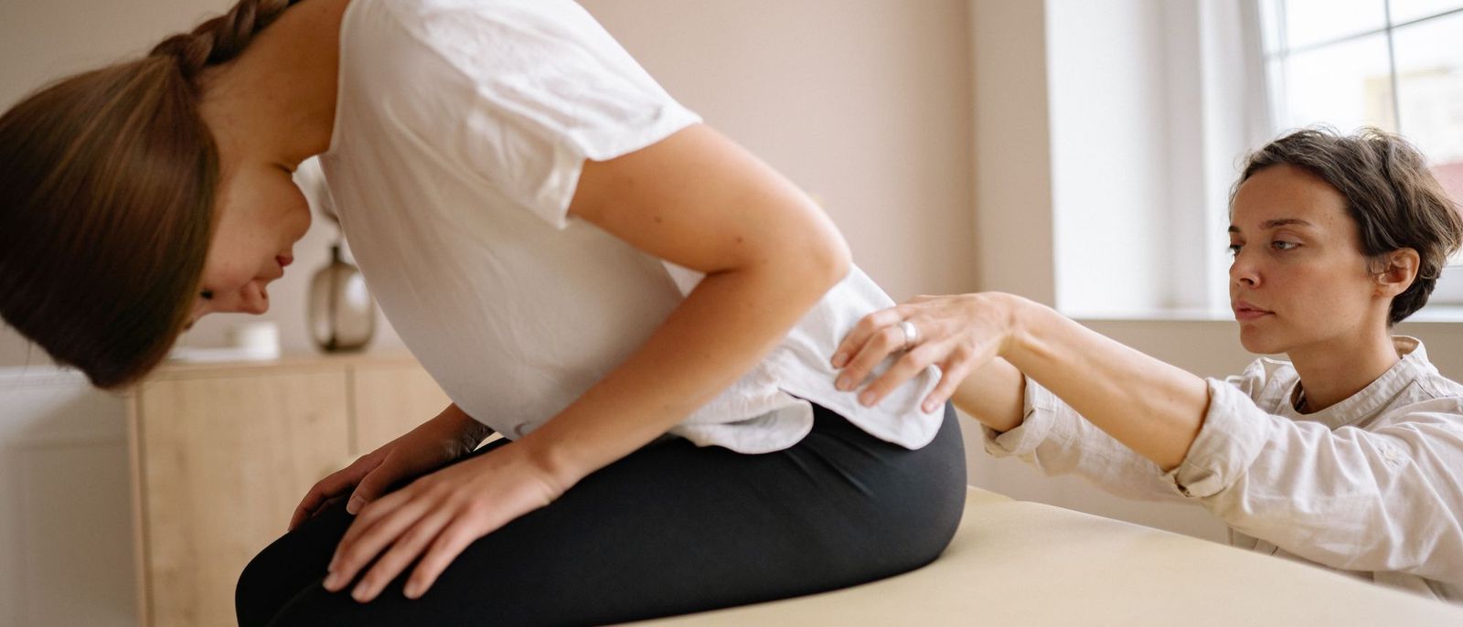 A therapist supports a patient through a seated lower back stretch.